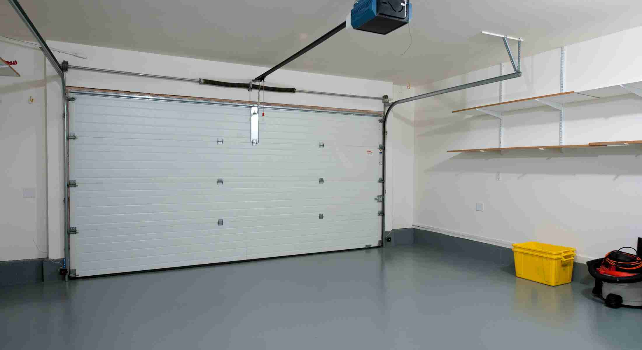 Interior view of a clean residential garage with a closed white sectional door, overhead opener, and grey epoxy flooring.